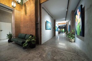 Un pasillo con un sofá verde, plantas en macetas y obras de arte en las paredes.
