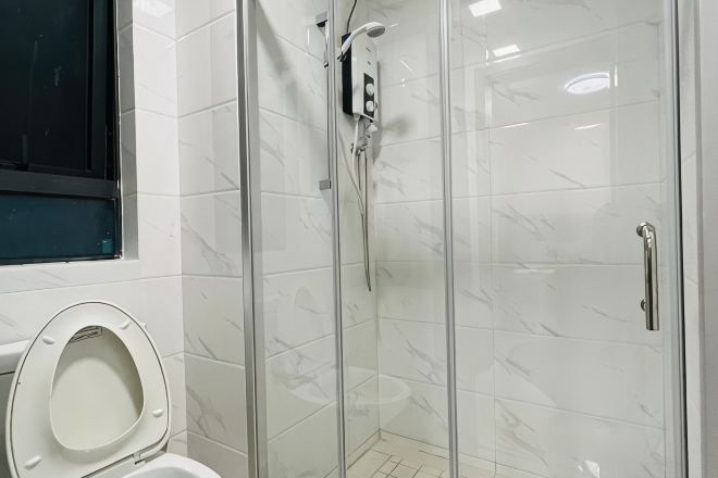 A bathroom with a toilet, a shower with a glass door, and a window.