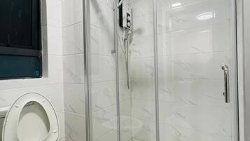 A bathroom with a toilet, a shower with a glass door, and a window.