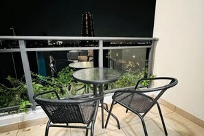 A balcony with a glass table and chairs, a railing, and a view of a cityscape at night. - Gelang Patah Forest City-Ataraxia Park 3 (Gelang Patah)