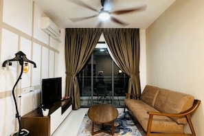 Un salon avec un canapé, un téléviseur, un ventilateur de plafond et une grande fenêtre avec des rideaux.