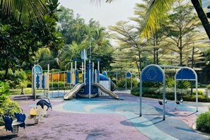 Ein Spielplatz mit Rutschen und Schaukeln, umgeben von viel Grün.