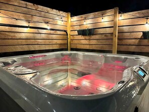 Un bain à remous avec un mur en bois en arrière-plan et des guirlandes lumineuses.