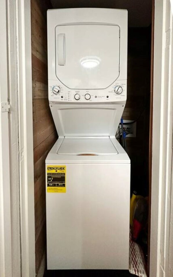 Un appareil combiné lave-linge et sèche-linge à chargement frontal, de couleur blanche, doté d’une étiquette « Guide énergétique », installé dans une buanderie aux murs en bois.