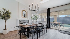 Un espace repas avec une table en bois, des chaises noires, un lustre et une vue sur une piscine.