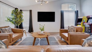 Un salon avec des canapés en cuir, une table basse, une grande plante et un téléviseur à écran plat fixé au mur.