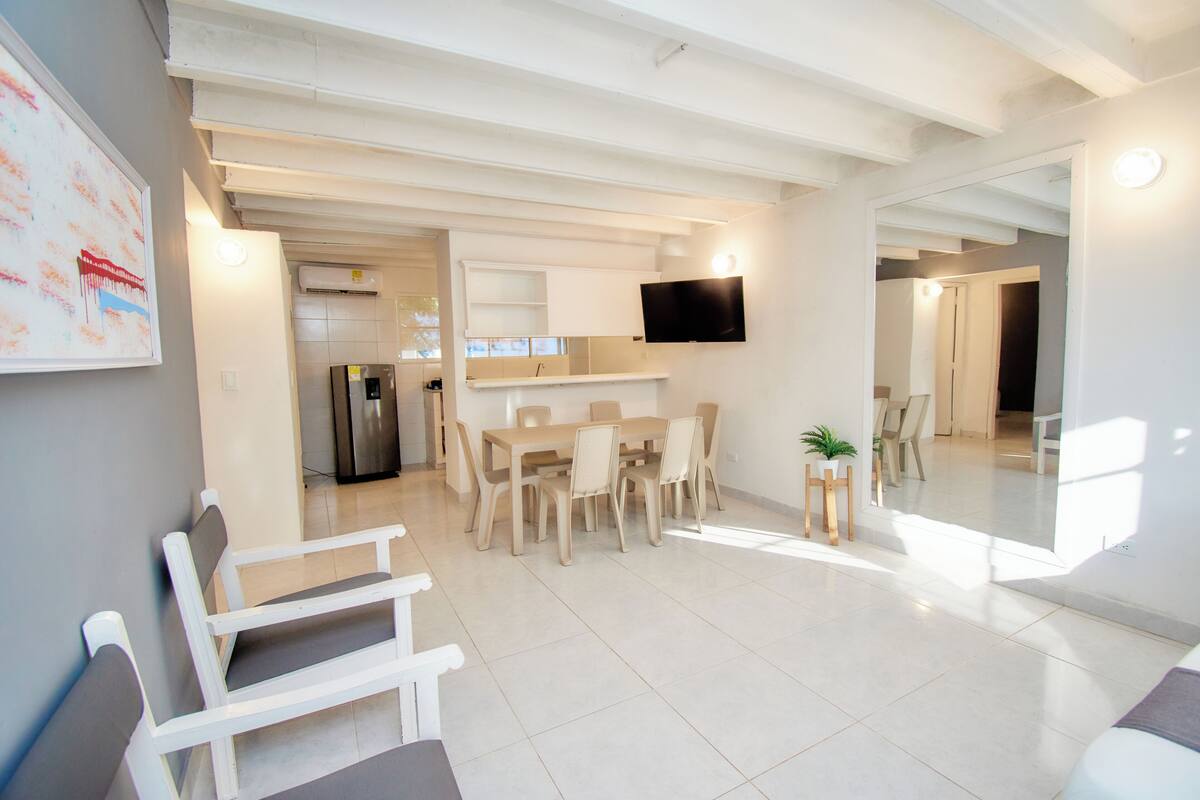 A modern living room with a dining area, a kitchen, and a TV mounted on the wall.