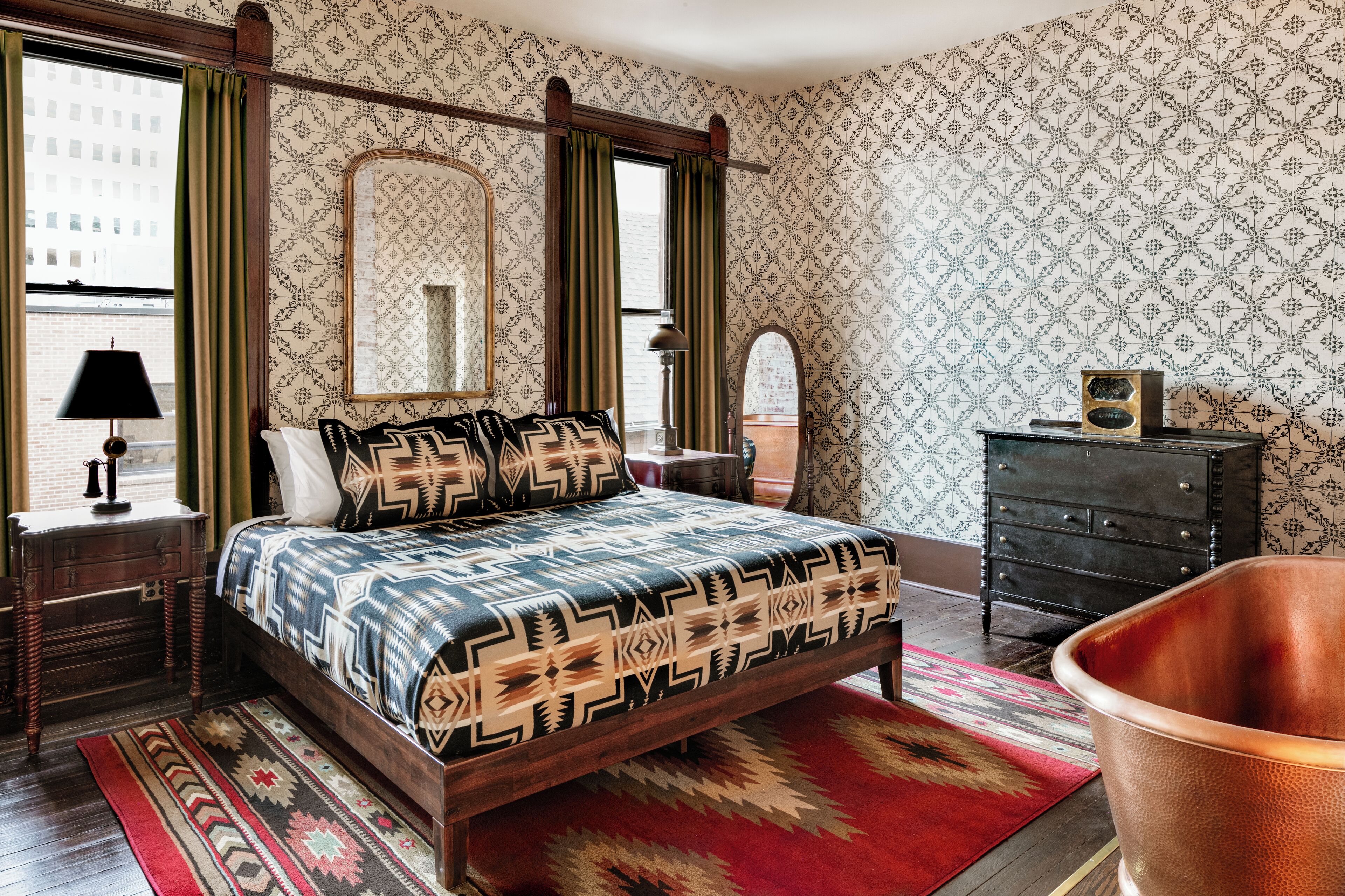A bedroom with a four-poster bed, a dresser, a mirror, and a copper bathtub.