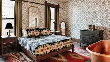 A bedroom with a four-poster bed, a dresser, a mirror, and a copper bathtub.