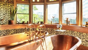 Une salle de bain au style rétro, avec une baignoire sur pieds, des motifs décoratifs élaborés sur les murs et de nombreuses fenêtres offrant une vue sur la ville.