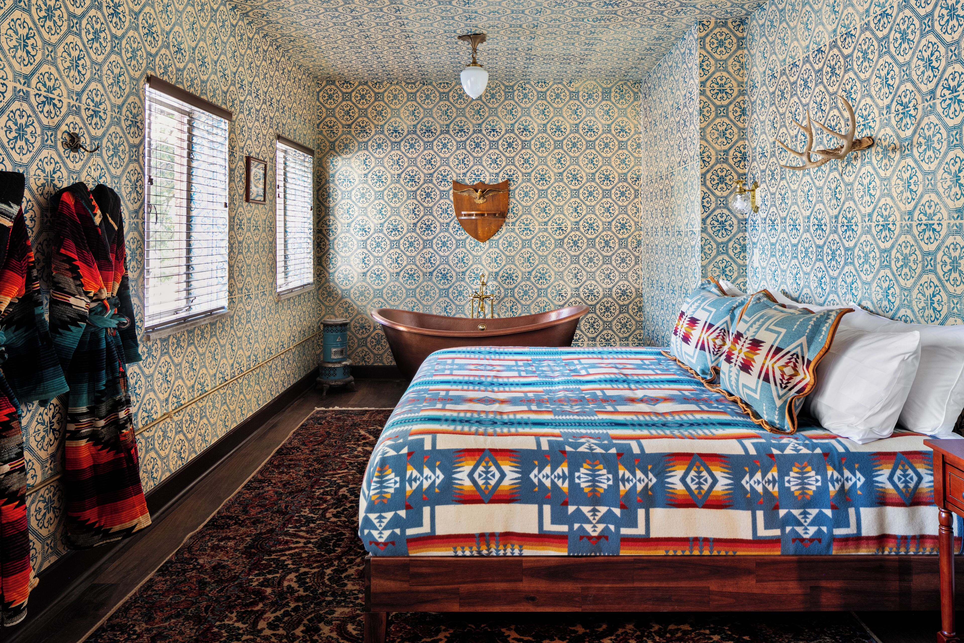 Una habitación con papel tapiz estampado, una cama con colcha estampada, un banco de madera y una bañera.