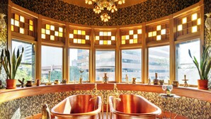 Une salle de bain d’angle avec deux vasques en cuivre, des encadrements de fenêtres décoratifs et un luminaire ornemental au plafond.