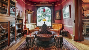Une pièce de style traditionnel, dotée d’une cheminée, de fauteuils en cuir, d’un tapis à motifs et d’une grande fenêtre offrant une vue sur les arbres.
