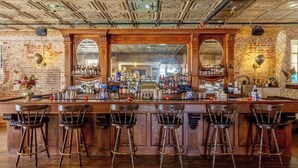 Un bar avec un mur en briques, un comptoir en bois et de nombreux tabourets.