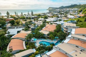 Un complejo turístico frente al mar con piscina rodeada de palmeras y vistas al océano.