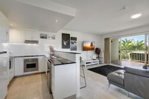 A modern kitchen with white cabinetry, a central island, and a dining area with a grey sofa.