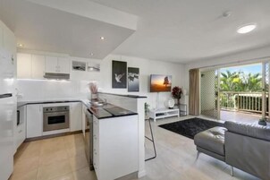 Una cocina moderna con armarios blancos, una isla central y un comedor con sofá gris.