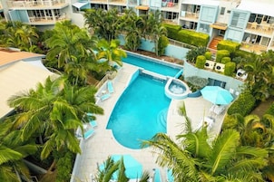Una piscina rodeada de palmeras y un edificio de hotel con balcones.