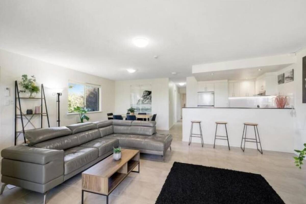 A modern living room with a sectional sofa, a small wooden table, and a black rug.