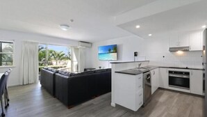 A modern kitchen with white cabinets, a built-in oven, and a dining area with a black table and chairs. - Lennox Beach Resort (Lennox Head)