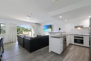 A modern kitchen with white cabinets, a built-in oven, and a dining area with a black table and chairs. - Lennox Beach Resort (Lennox Head)
