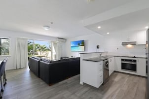 Una cocina moderna con armarios blancos, horno empotrado y comedor con una mesa y sillas negras.