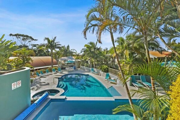 A swimming pool with a slide, surrounded by palm trees and lounge chairs.