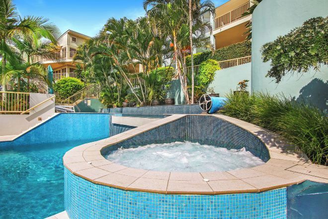 A swimming pool with a hot tub, surrounded by palm trees and a building with balconies.
