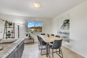 A dining area with a table and chairs, a sofa, a window with a view, and a plant. - Lennox Beach Resort (Lennox Head)