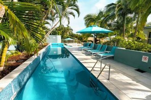 A swimming pool with lounge chairs and umbrellas, surrounded by palm trees and greenery. - Lennox Beach Resort (Lennox Head)