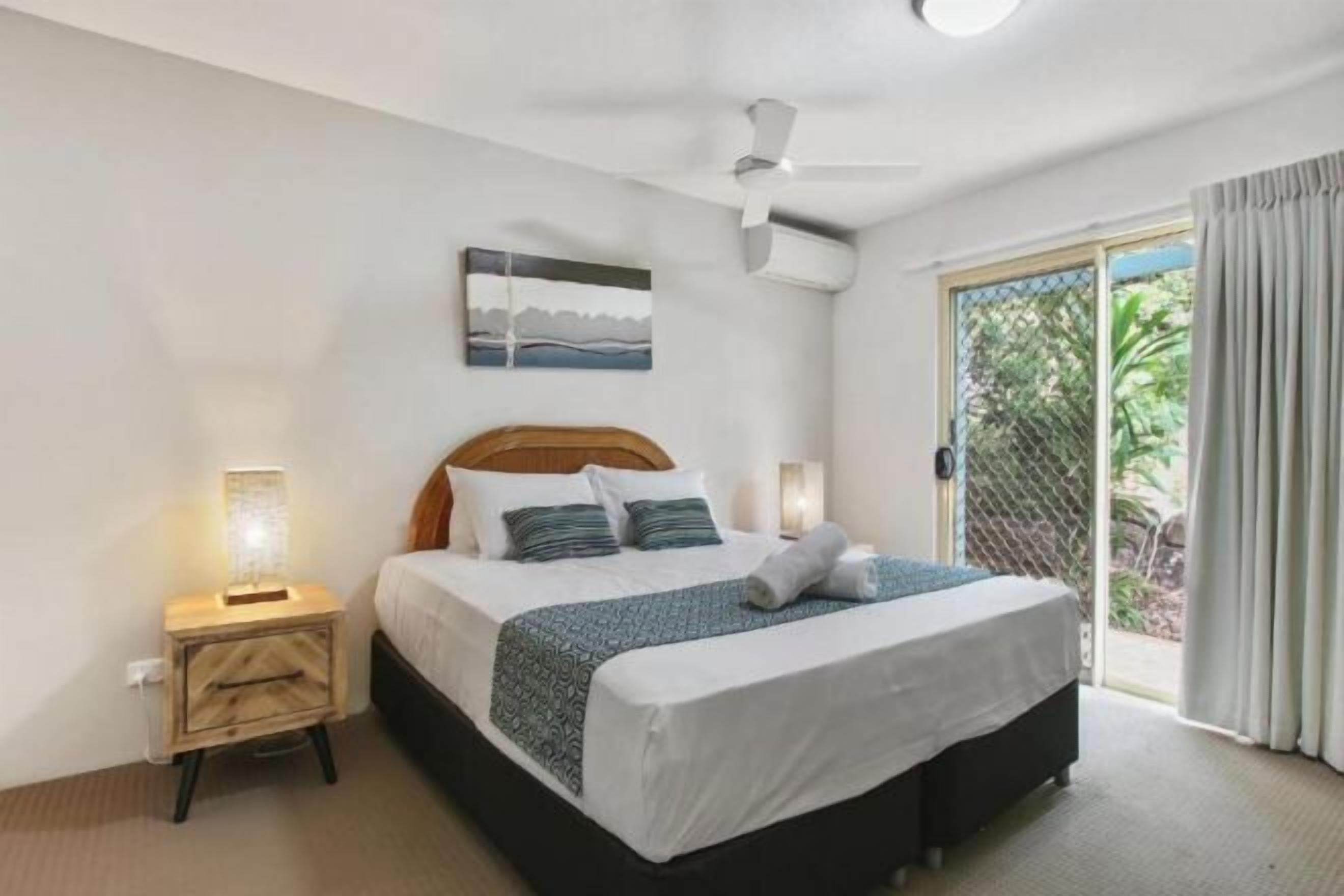 Un dormitorio con cama, mesita de noche y ventilador de techo.