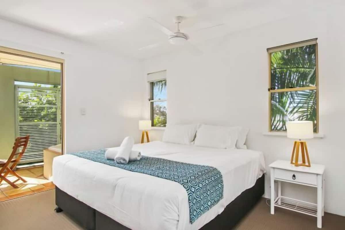 A bedroom with a bed, bedside tables, a ceiling fan, a window, and a door.