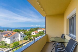 A balcony with a glass table and chairs, offering a view of a coastal town and mountains. - Studio Tena 1 with a sea view (Njivice)
