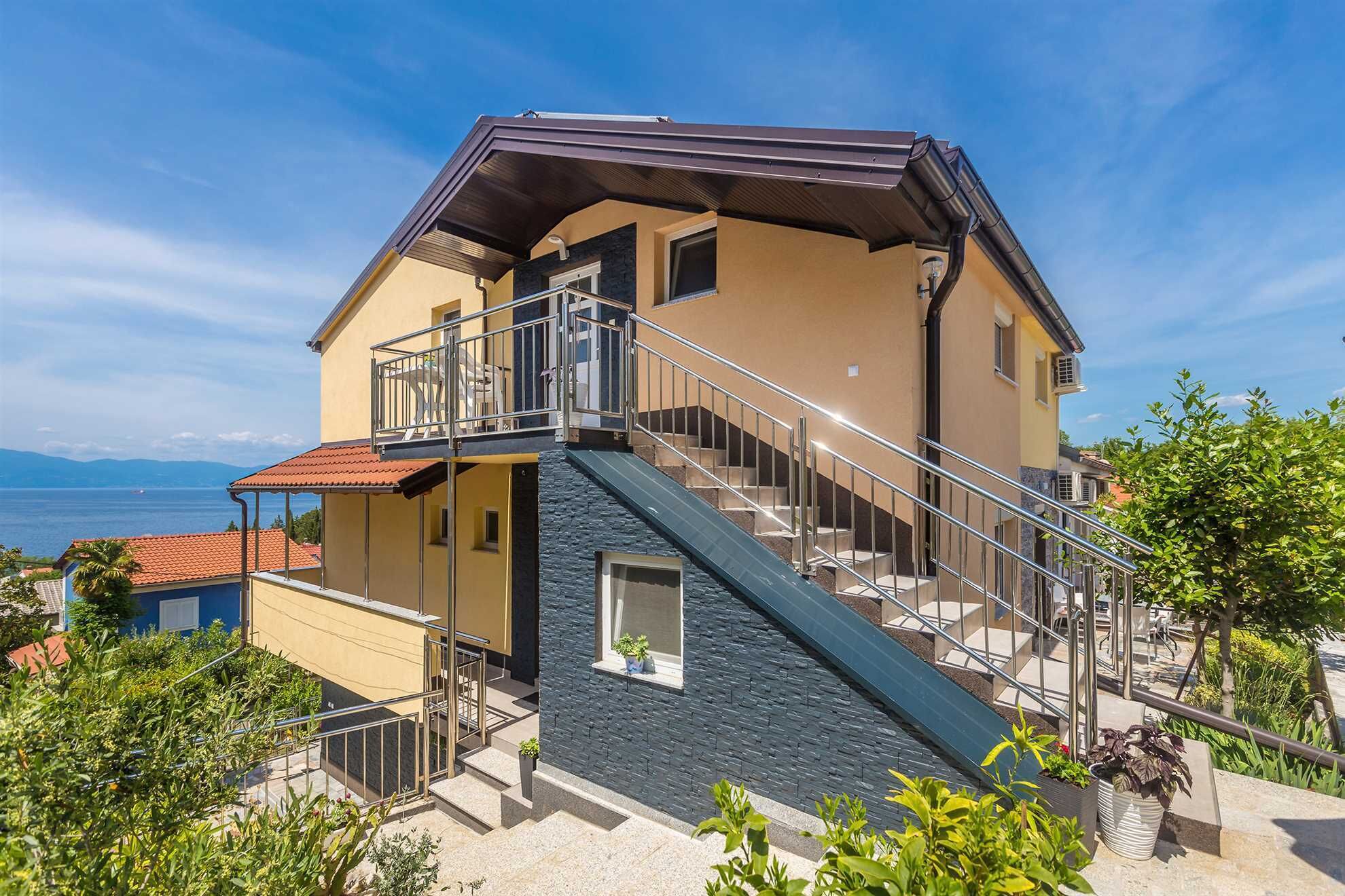 Une maison à deux étages avec un balcon, un escalier et une vue sur la mer.