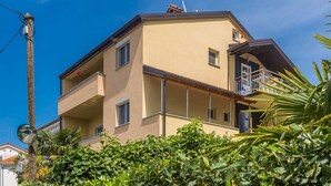 Un immeuble à plusieurs étages doté de balcons, d’une antenne parabolique bien visible et d’une végétation luxuriante au premier plan.
