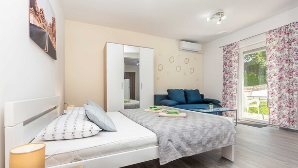 Une chambre moderne avec un lit, un canapé bleu, une petite table et une grande fenêtre avec des rideaux.