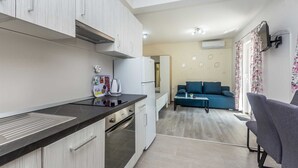 Une cuisine compacte avec un plan de travail noir, des placards blancs et un coin café. Un canapé bleu et un fauteuil gris se trouvent dans l’espace salon.
