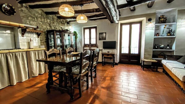 A dining area with a wooden table and chairs, a stone wall, and a hanging light fixture. - CAN PINÓS DE GUIMERÀ (Guimerà)