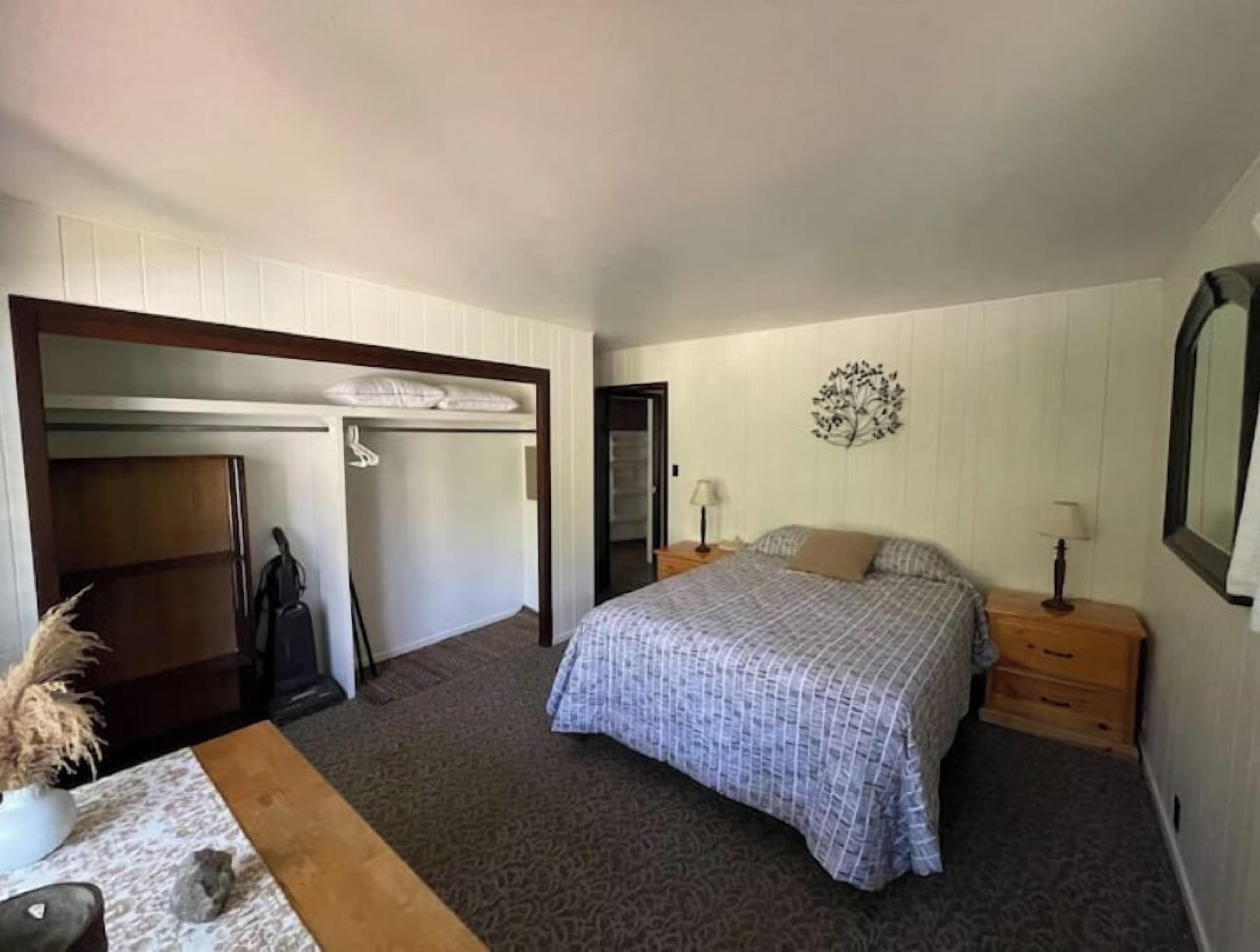 Un dormitorio con cama, mesita de noche, cómoda, armario y un adorno en la pared.