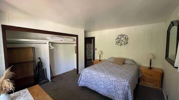 Un dormitorio con cama, mesita de noche, cómoda, armario y un adorno en la pared.