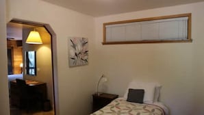 Ein Schlafzimmer mit Bett, Schreibtisch und Stuhl. Ein Fenster mit Jalousien und ein Bild an der Wand.