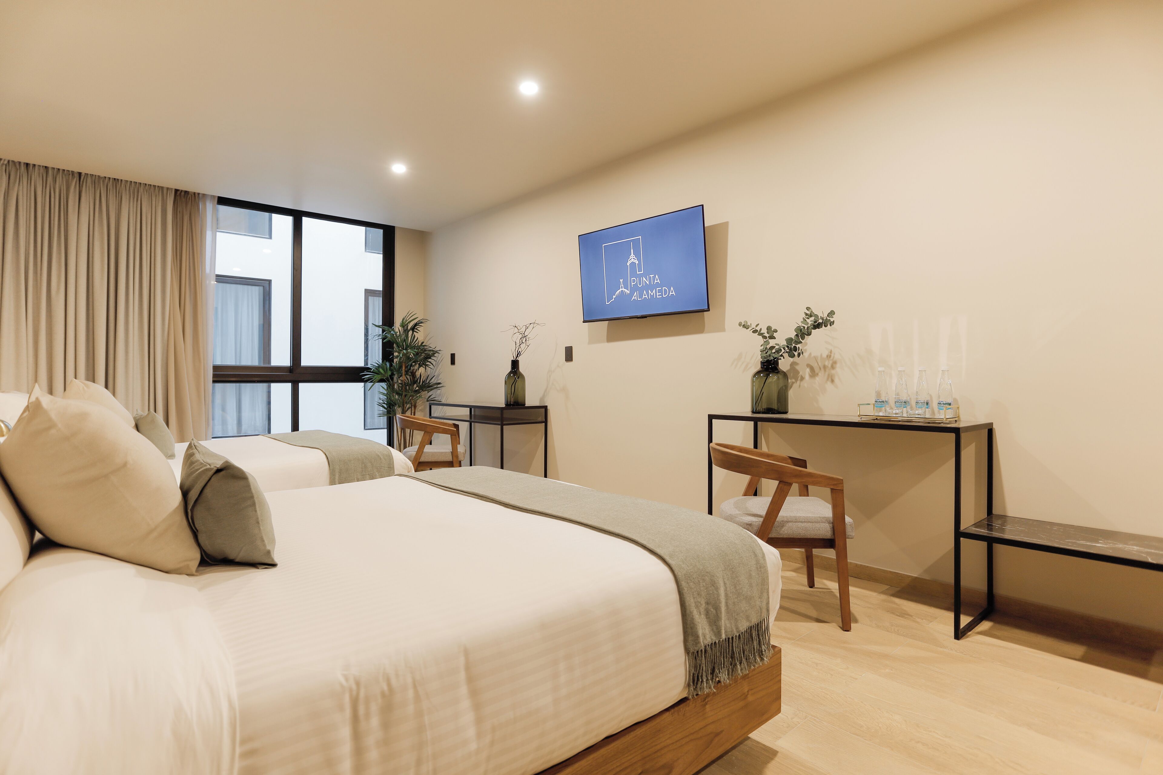 A modern hotel room with a large bed, a desk, and a television displaying 'Punta Alamedas'.