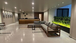 Un hall d’entrée moderne comprenant un comptoir d’accueil, un espace détente avec un canapé et des fauteuils, et une vue sur la verdure par une fenêtre.