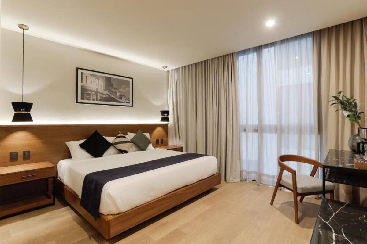 A modern hotel room with a large bed, bedside tables, a desk, and a chair.