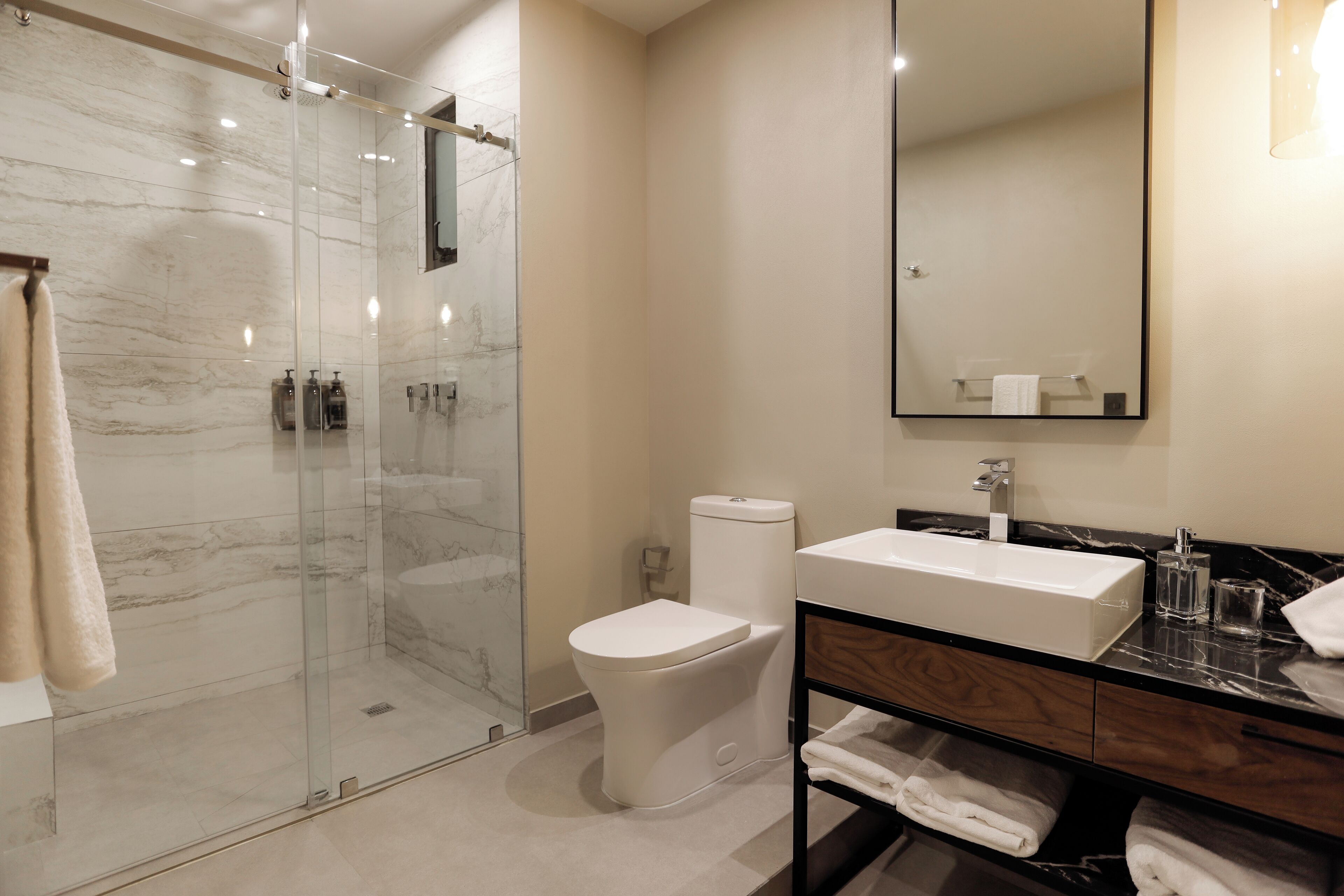 A modern bathroom with a glass-enclosed shower, a white toilet, a sink with a marble countertop, and a mirror above the sink.