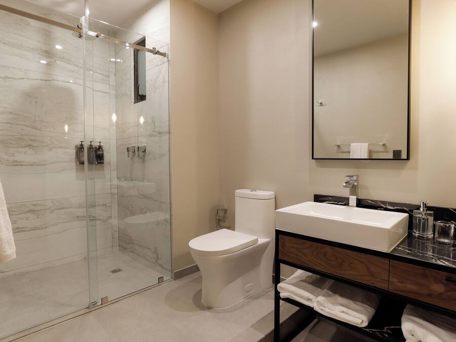 A modern bathroom with a glass-enclosed shower, a white toilet, a sink with a marble countertop, and a mirror above the sink.