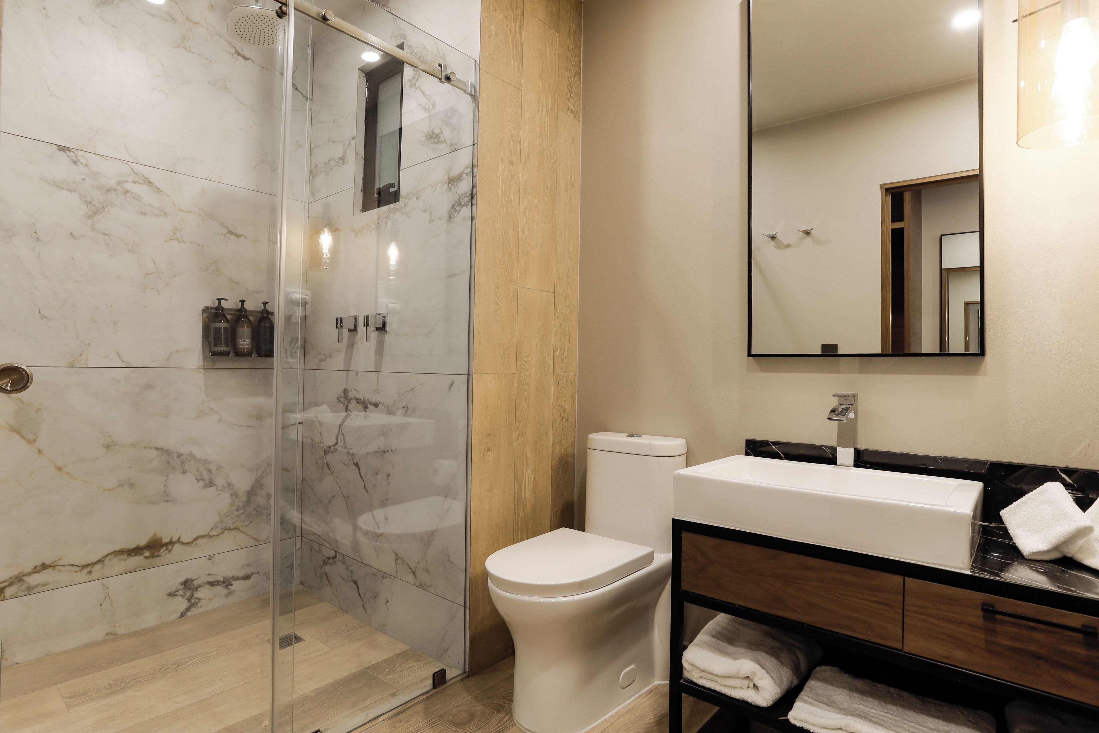 Een moderne badkamer met een glazen douchecabine, een wit toilet en een wastafel met spiegel.