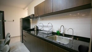 A modern kitchen with dark wooden cabinets, a stainless steel sink, and a black countertop. - Paradise Suite at KK Times Square, Beside Imago (Kota Kinabalu)