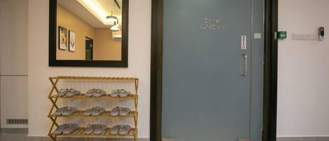 Un pasillo con un zapatero, una puerta con un letrero y un espejo que refleja el interior.