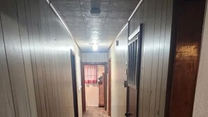 Un pasillo estrecho con paredes de madera y suelo de baldosas, que conduce a una habitación con una cortina roja.